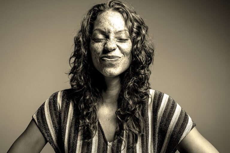 Black and white portrait of a woman with curly hair scrunching up her face with her eyes shut