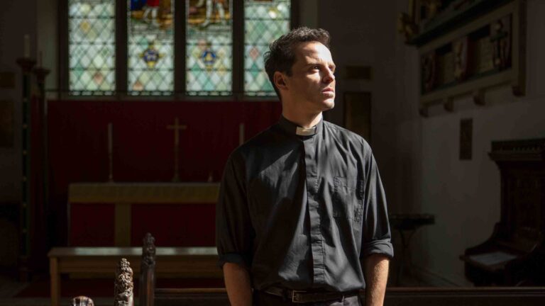 A man in a black clerical shirt and collar standing in a church, looking up towards the light
