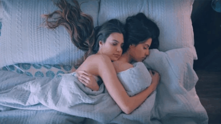Two women asleep in each other's arms under a pale blue duvet