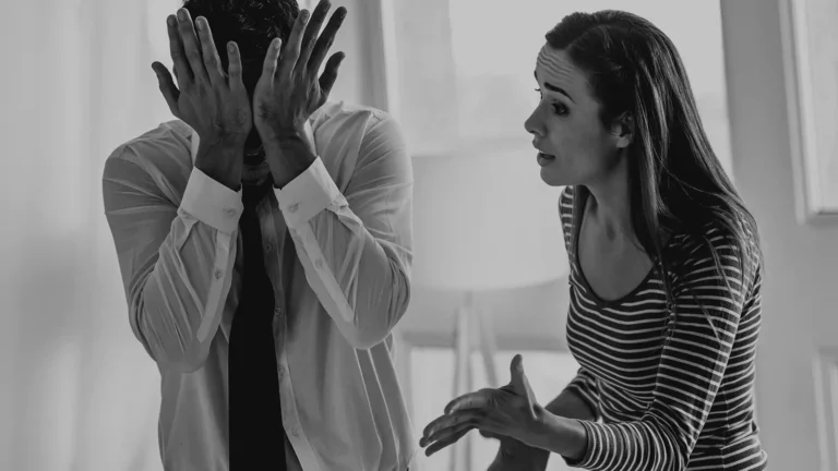A black and white photo of a couple arguing, the man covering his face with his hands while the woman gestures as she speaks
