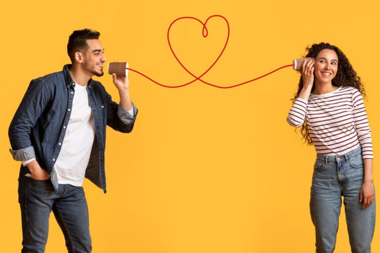 A man and a woman talking through tin can telephones joined by a red string looped into a heart, on a yellow background